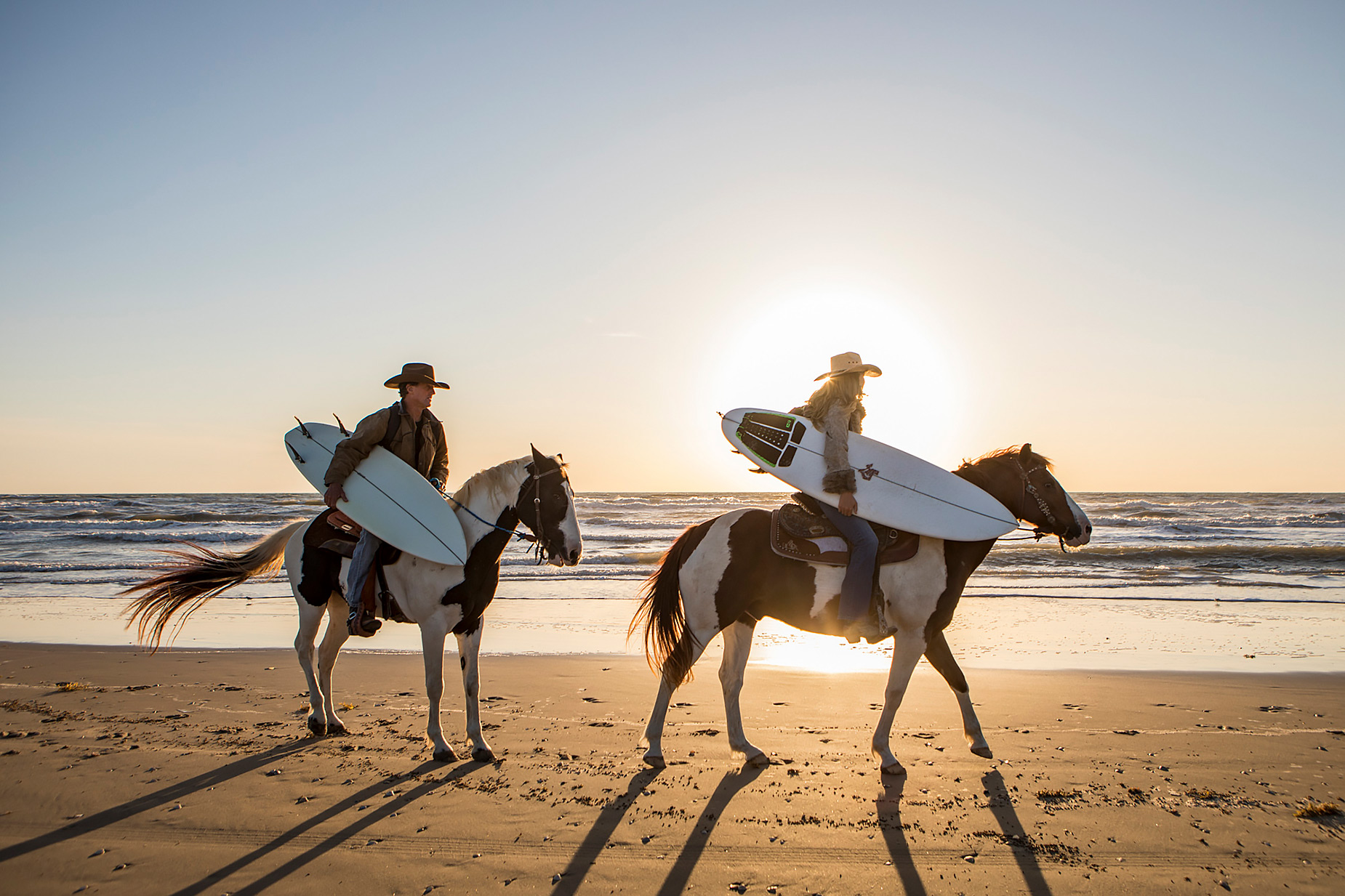 Texas surfers on horseback on the beach at sunrise